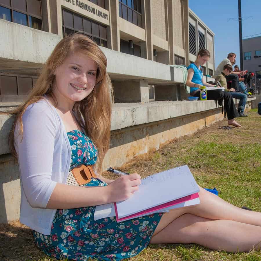 A student sitting outside in the sun and taking notes